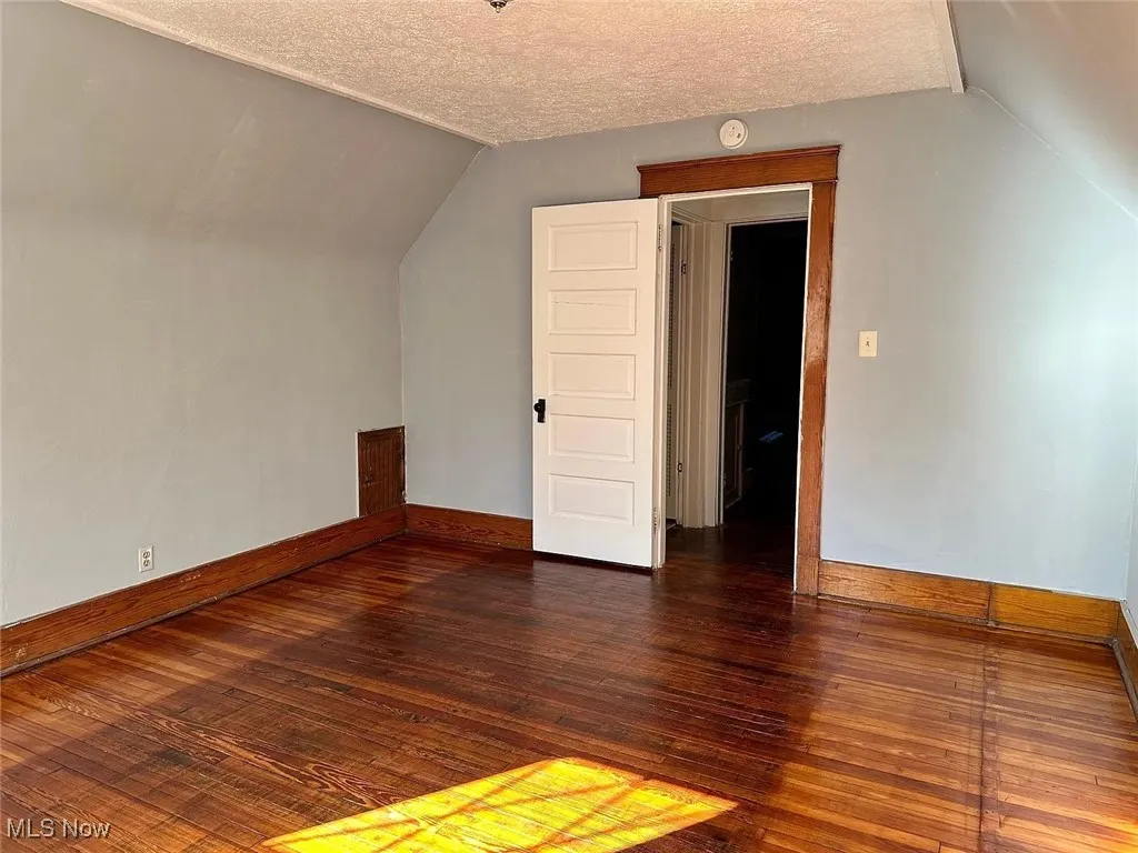 Unit 2: Bedroom space with lofted ceiling, wood-type flooring, baseboards, and a textured ceiling