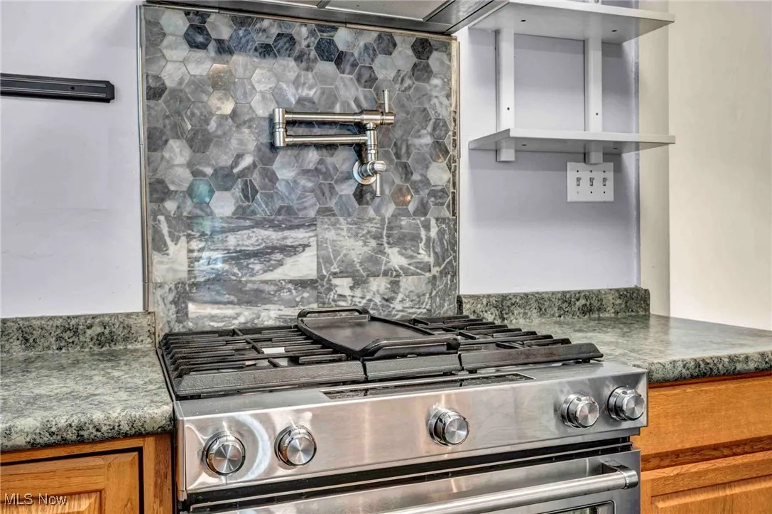 Kitchen featuring stainless steel gas range oven, brown cabinetry, and dark countertops