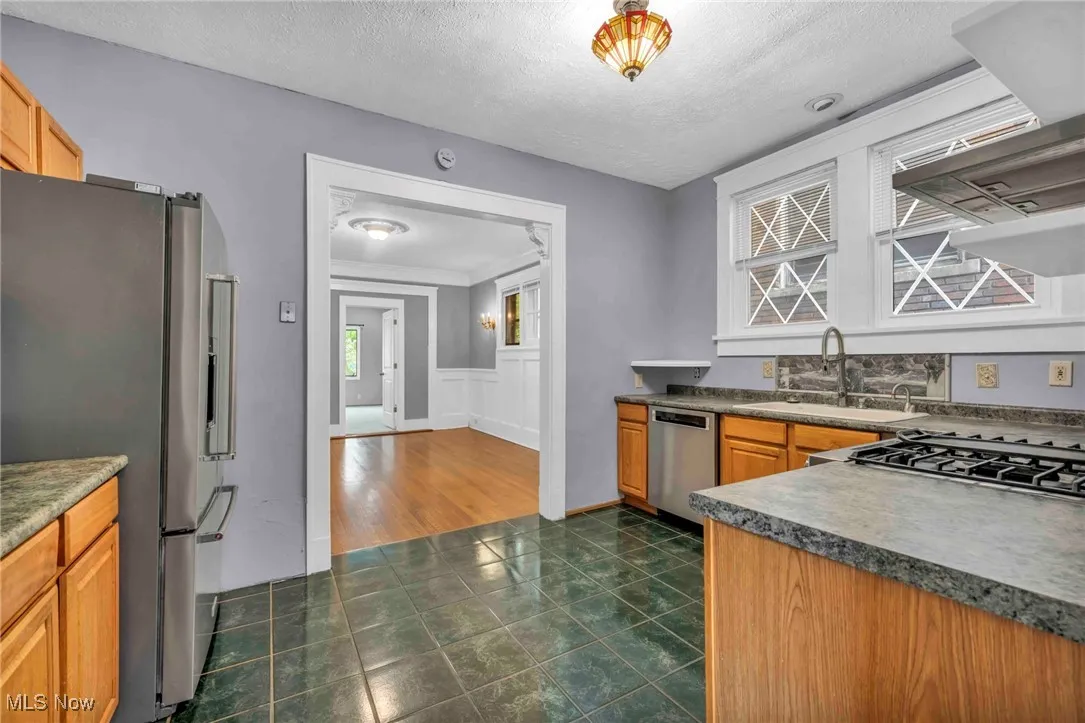 Kitchen featuring appliances with stainless steel finishes, a sink, a textured ceiling, exhaust hood, and dark countertops