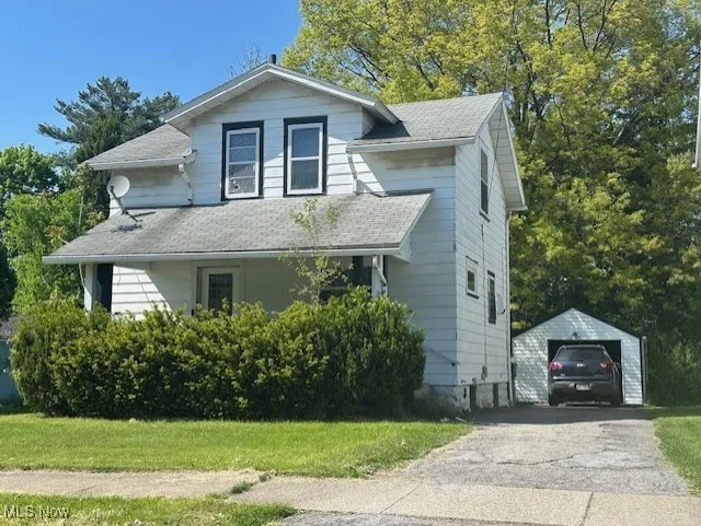 View of front facade featuring an outbuilding, a garage, roof with shingles, and asphalt driveway