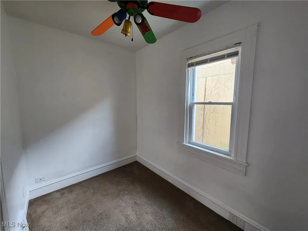 Spare room with dark carpet, ceiling fan, and baseboards