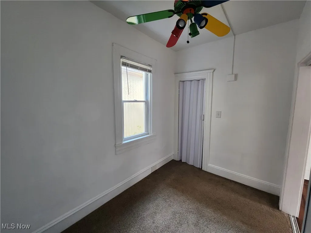 Empty room featuring ceiling fan, dark carpet, and baseboards