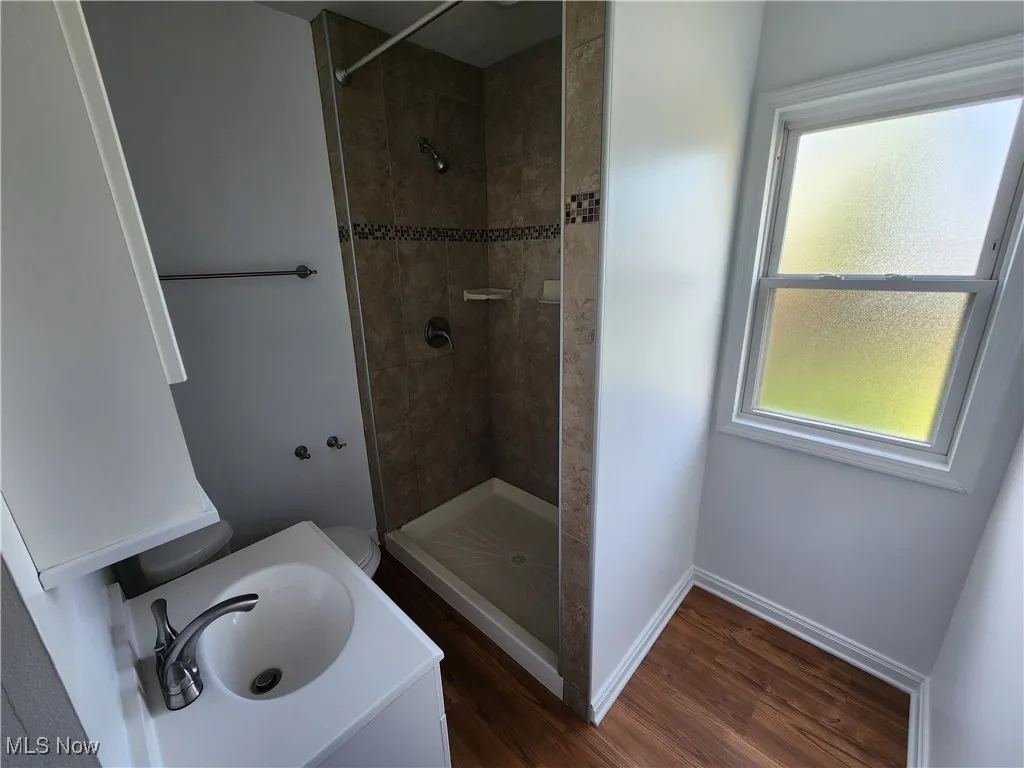 Bathroom featuring tiled shower, wood finished floors, a sink, and baseboards