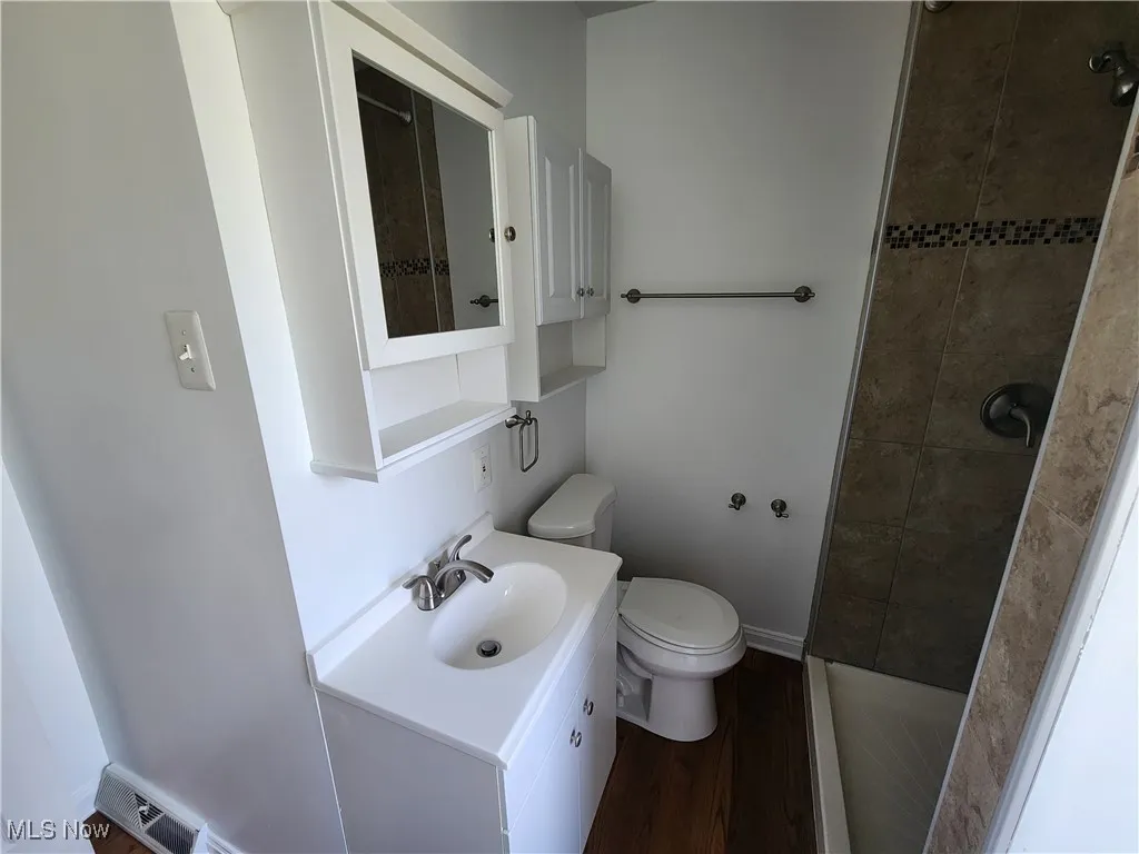 Full bath featuring toilet, a tile shower, vanity, and wood finished floors