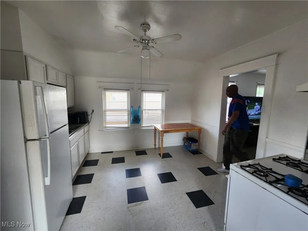 Kitchen with white appliances, lofted ceiling, light flooring, a ceiling fan, and baseboards