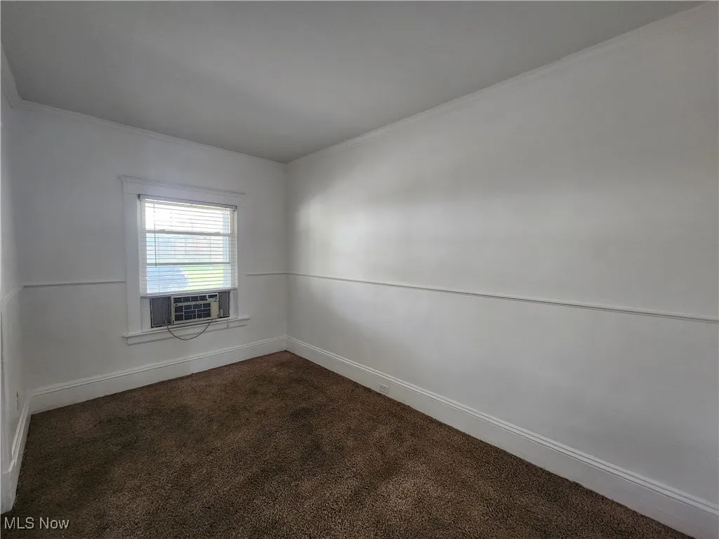 Unfurnished room featuring dark colored carpet, ornamental molding, cooling unit, and baseboards