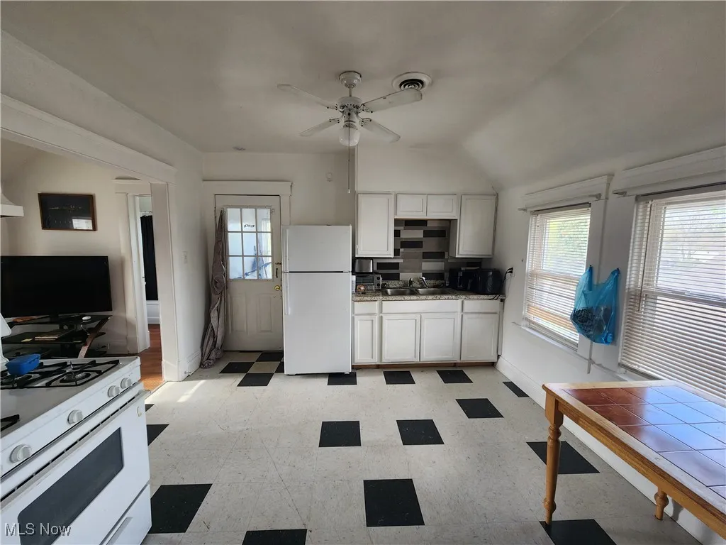 Kitchen with white appliances, light flooring, a ceiling fan, baseboards, and white cabinetry