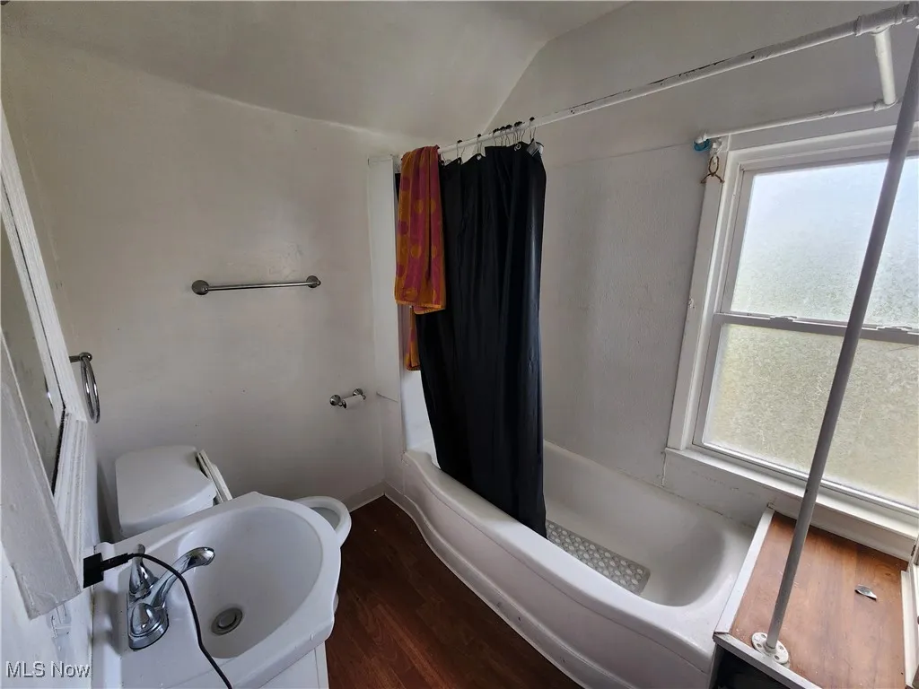 Full bathroom with wood finished floors, vaulted ceiling, toilet, shower / bath combination with curtain, and baseboards