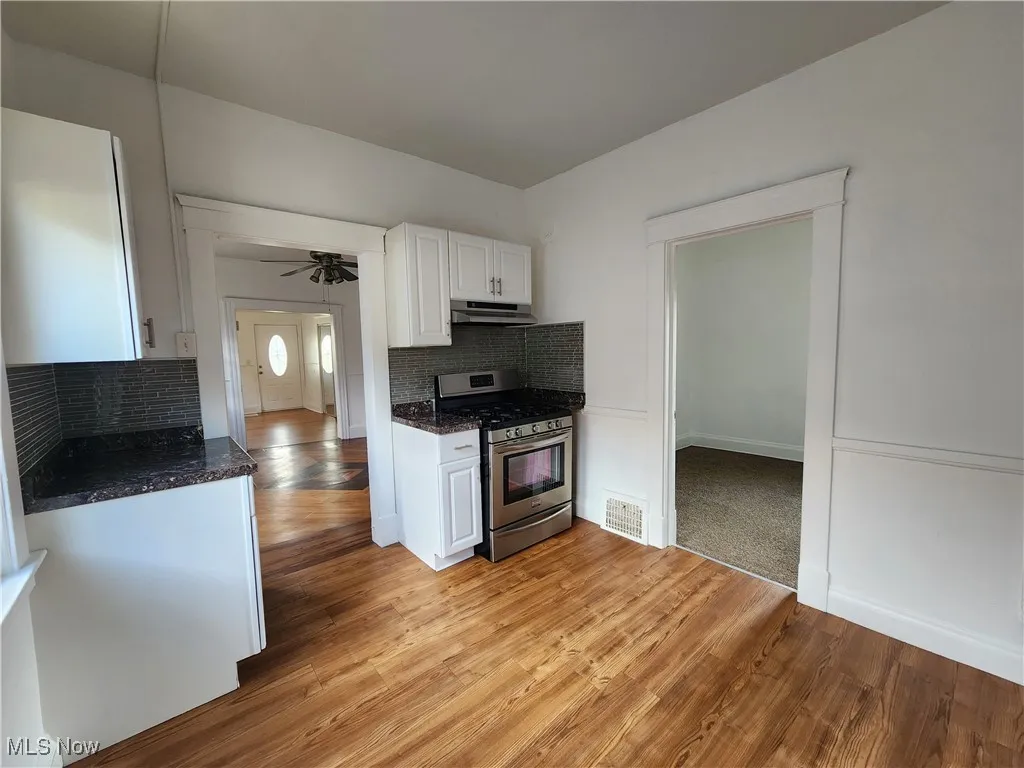 Kitchen featuring stainless steel gas range oven, under cabinet range hood, white cabinetry, tasteful backsplash, and light wood-type flooring
