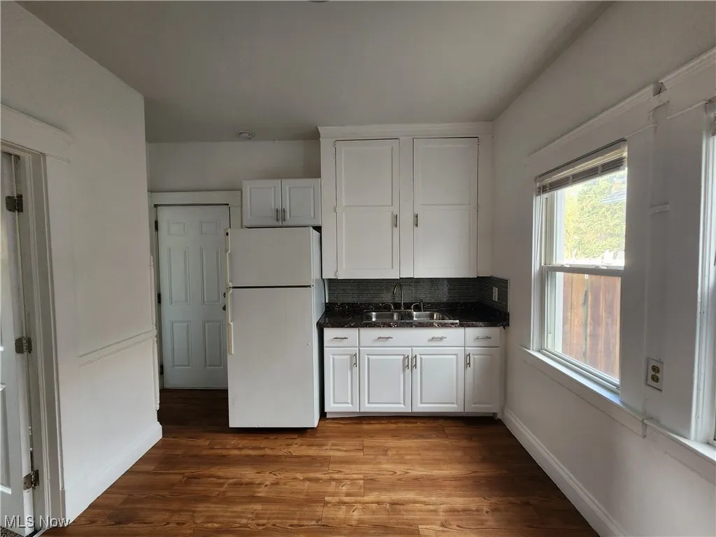Kitchen with freestanding refrigerator, a sink, white cabinetry, and wood finished floors
