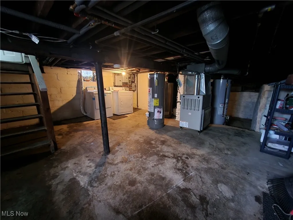 Unfinished basement featuring water heater, washing machine and dryer, heating unit, and stairway