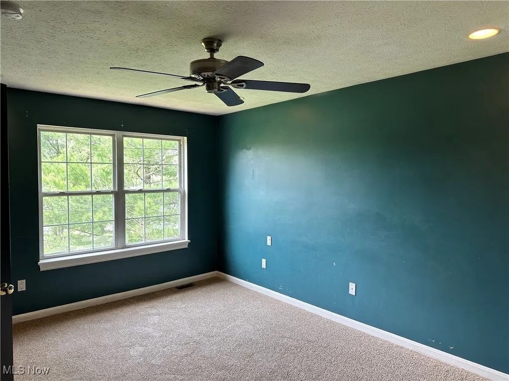 Carpeted empty room featuring baseboards, a textured ceiling, a smoke detector, and ceiling fan