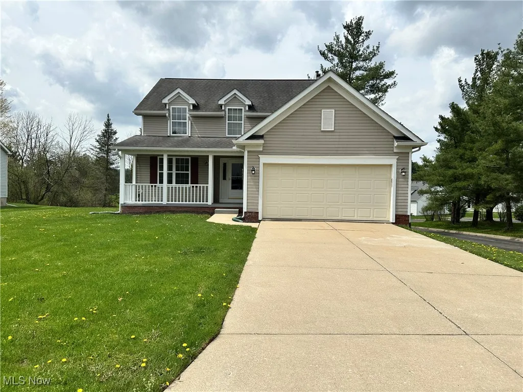 Traditional-style house with covered porch, driveway, a front lawn, a garage, and a shingled roof
