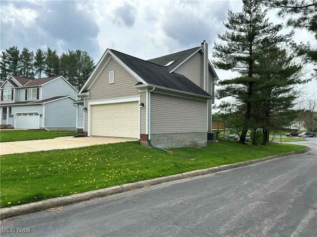View of property exterior featuring a chimney, concrete driveway, a lawn, and central AC unit