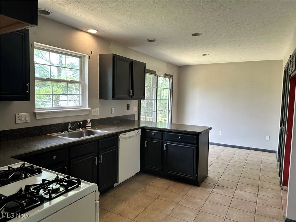 Kitchen featuring white appliances, dark countertops, a textured ceiling, dark cabinets, and light tile patterned flooring