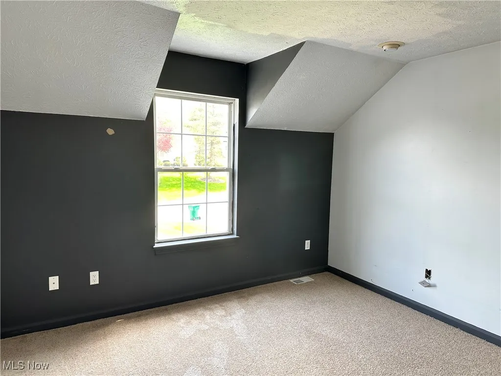 Bonus room featuring a textured ceiling, carpet floors, vaulted ceiling, and baseboards