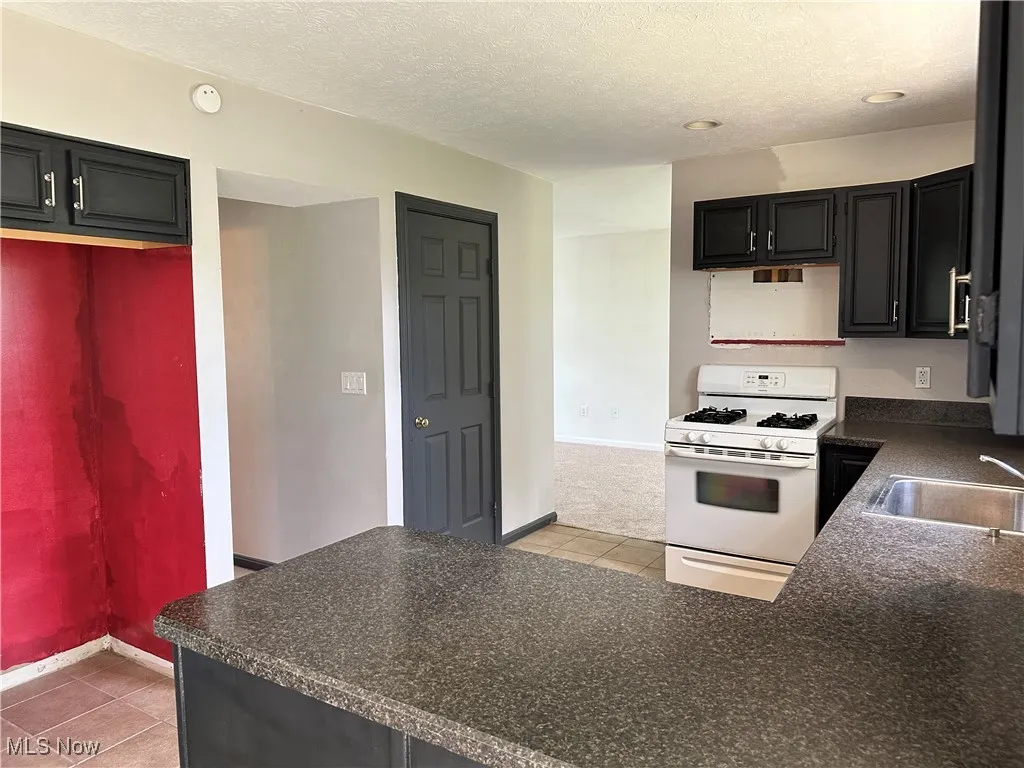 Kitchen featuring white gas range, a sink, dark countertops, baseboards, and a textured ceiling