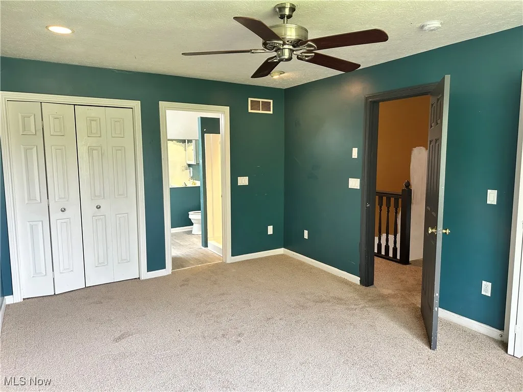 Unfurnished bedroom featuring carpet, baseboards, a closet, connected bathroom, and a textured ceiling