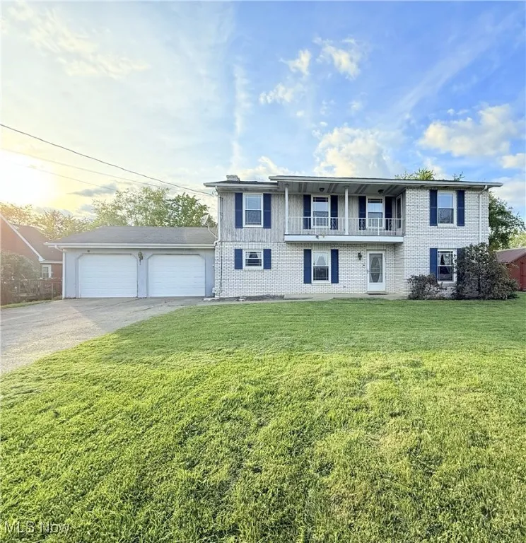 View of front featuring a balcony, a front lawn, concrete driveway, and a garage