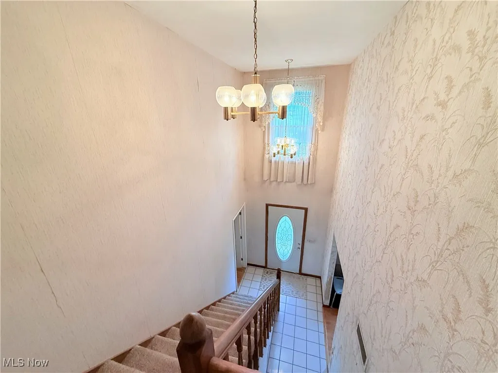 Tiled foyer entrance with a chandelier, stairs, and wallpapered walls