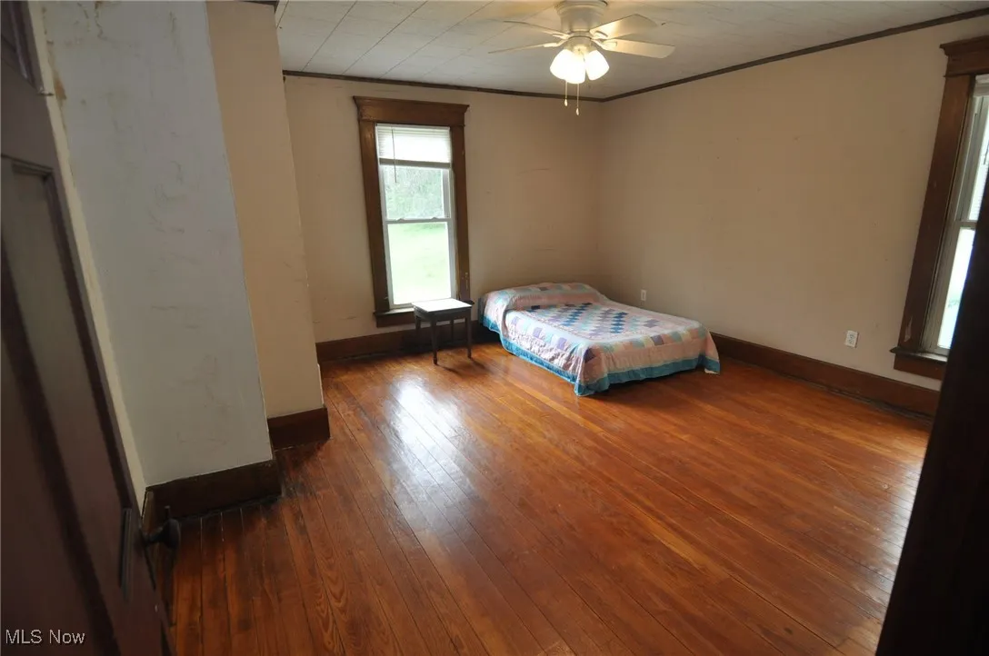Second floor bedroom featuring ornamental molding, hardwood / wood-style floors, baseboards, and ceiling fan