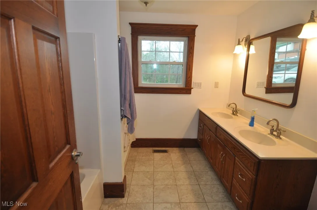 First floor full bath with baseboards, a shower with shower curtain, separate tub, double vanity, and tile patterned floors