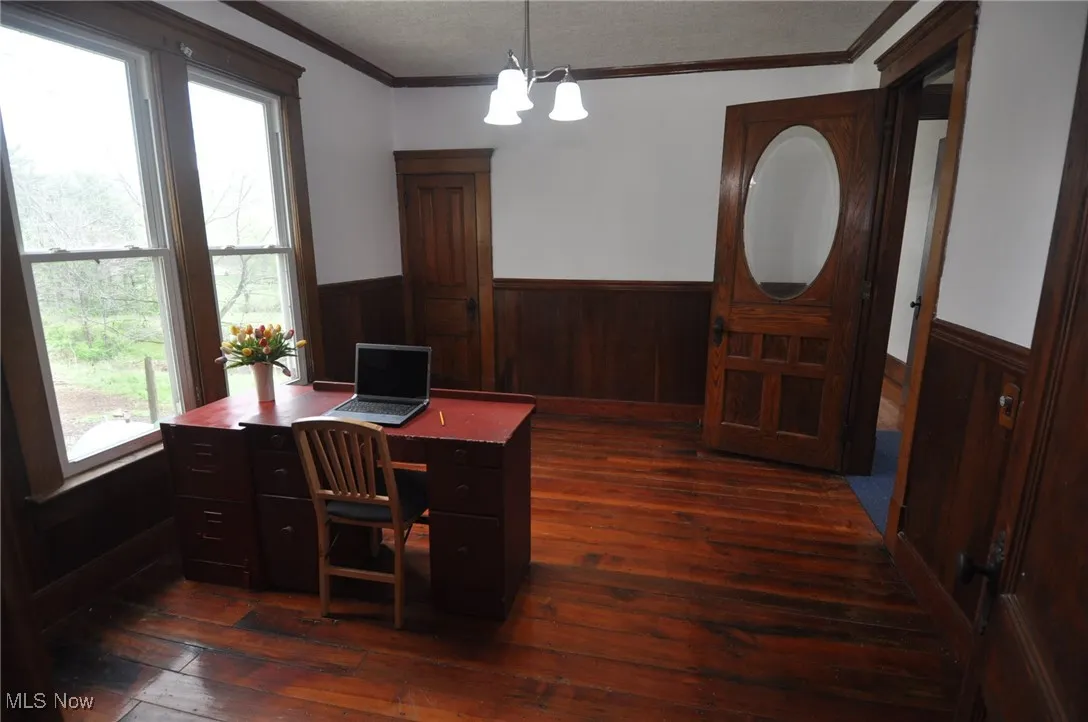 Second view of the library/office space featuring wainscoting, dark wood-style floors, crown molding, and wood walls