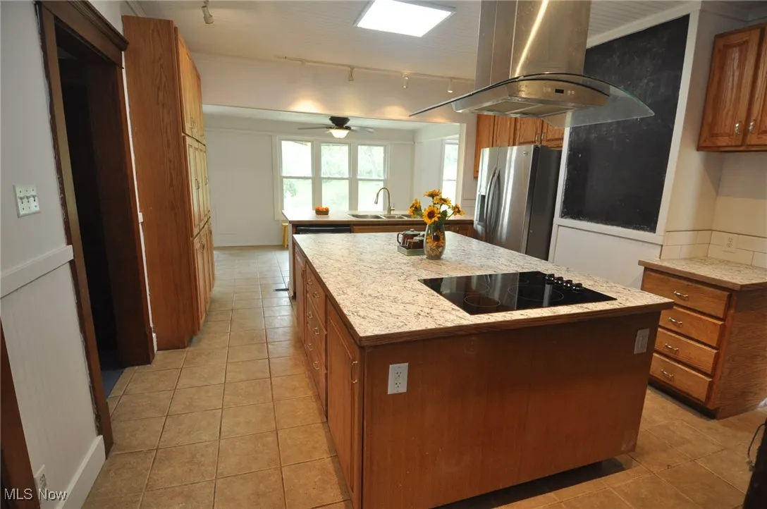Kitchen featuring stainless steel fridge with ice dispenser, black electric stovetop, island exhaust hood, brown cabinetry, and rail lighting