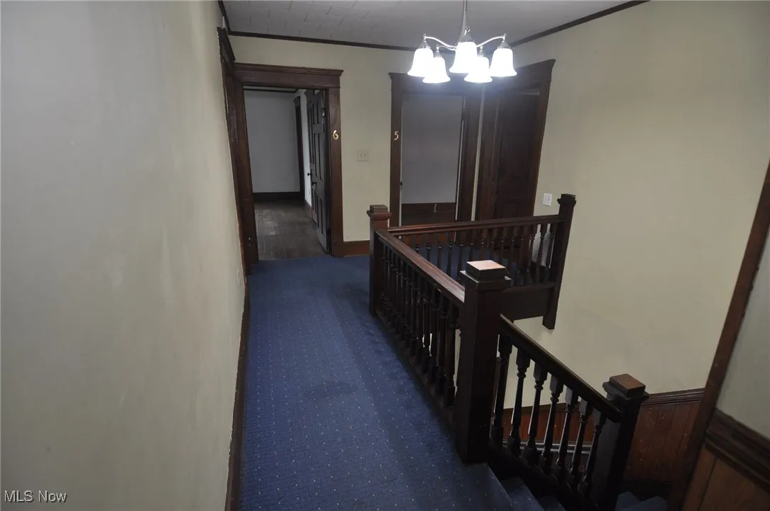 Hall with an upstairs landing, ornamental molding, and carpet flooring