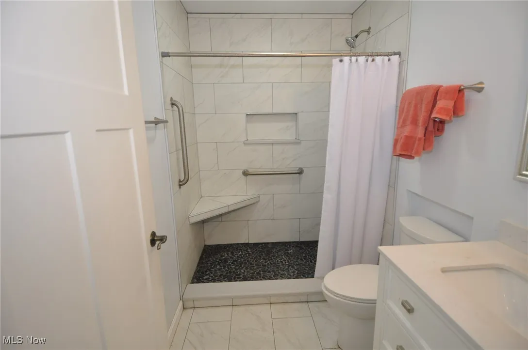 Bungalow full bath with ceramic finish floors, toilet, a tile shower, and vanity