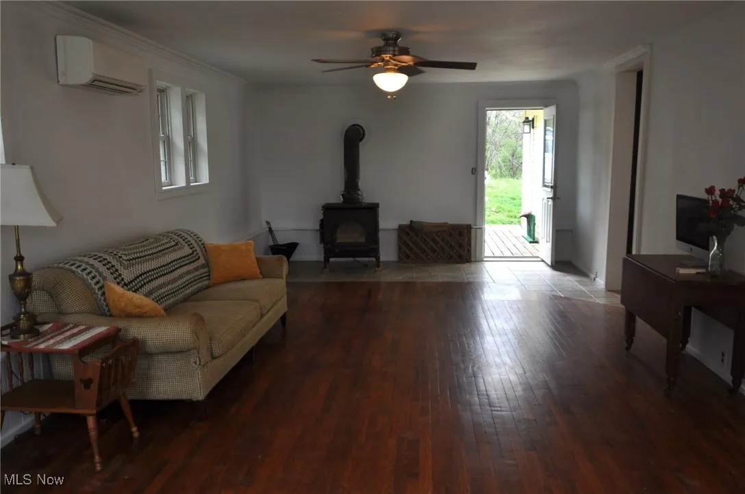 Family room featuring a wall unit AC, a wood stove, hardwood / wood-style flooring, and a ceiling fan
