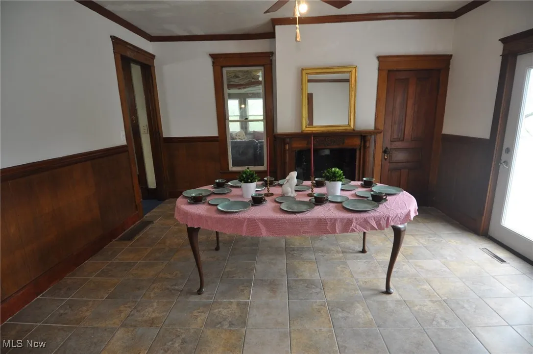 Dining room with decorative fireplace, a wainscoted wall, plenty of natural light, ceiling fan, wood walls, and ornamental molding