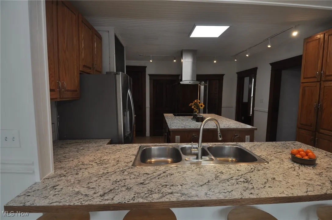 Kitchen featuring rail lighting, freestanding refrigerator, a sink, a center island, and a peninsula