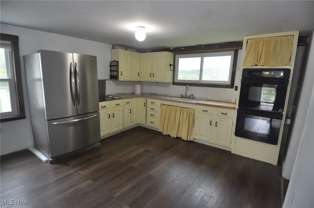 Bungalow kitchen with freestanding refrigerator, a sink, dark wood-style flooring, and cream cabinets
