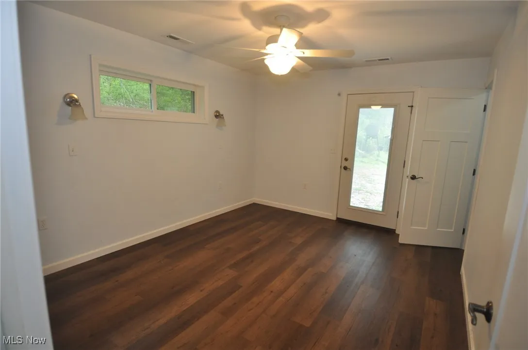 Bungalow bedroom with door outside and dark wood-style floors, baseboards, and a ceiling fan