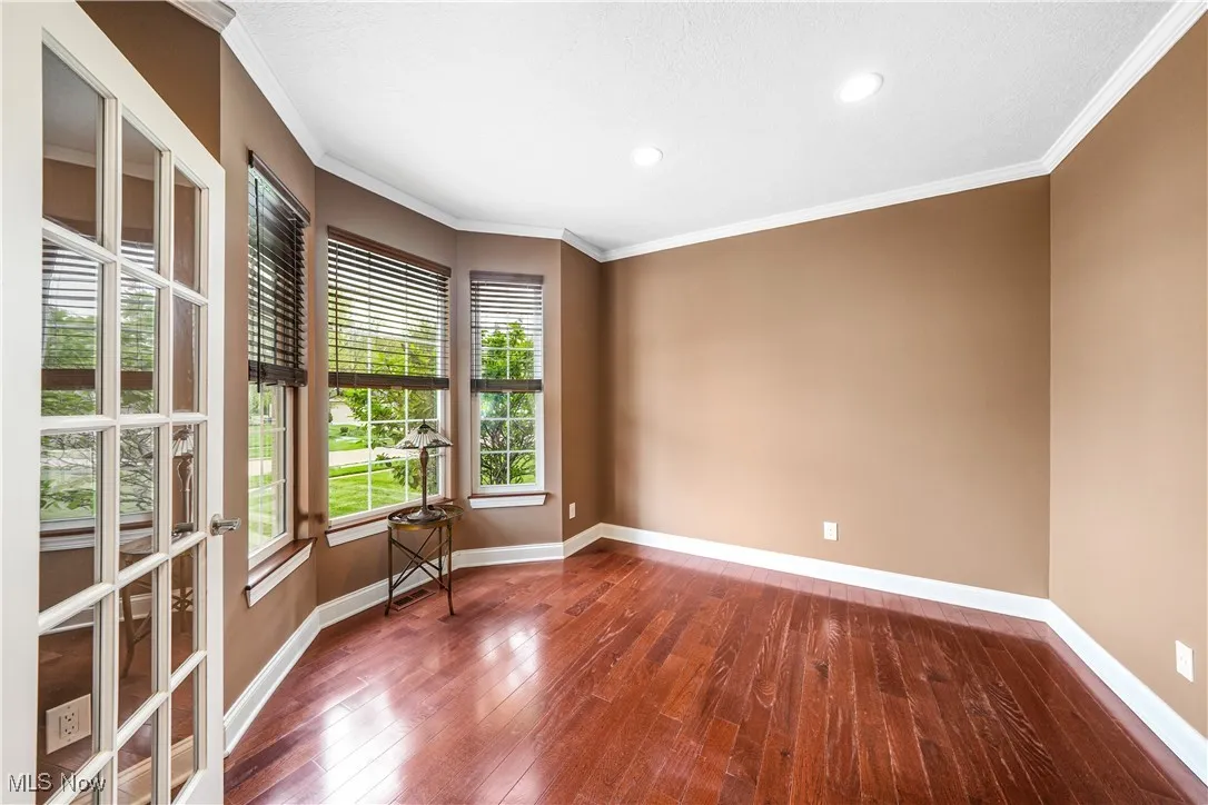 Empty room featuring hardwood / wood-style floors, baseboards, crown molding, and recessed lighting