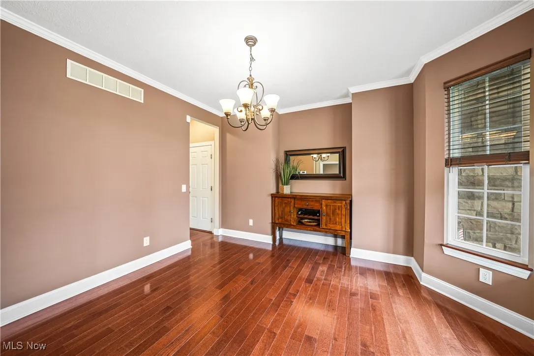 Unfurnished dining area with a chandelier, hardwood / wood-style floors, baseboards, and crown molding