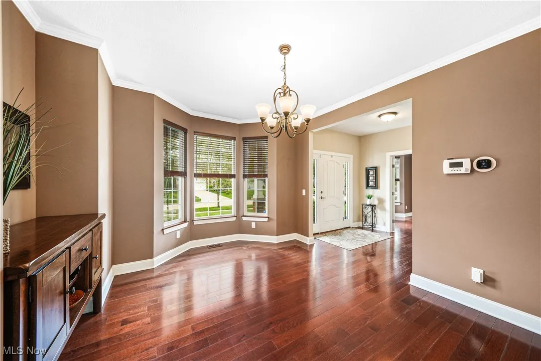 Unfurnished dining area featuring a chandelier, baseboards, wood finished floors, and ornamental molding
