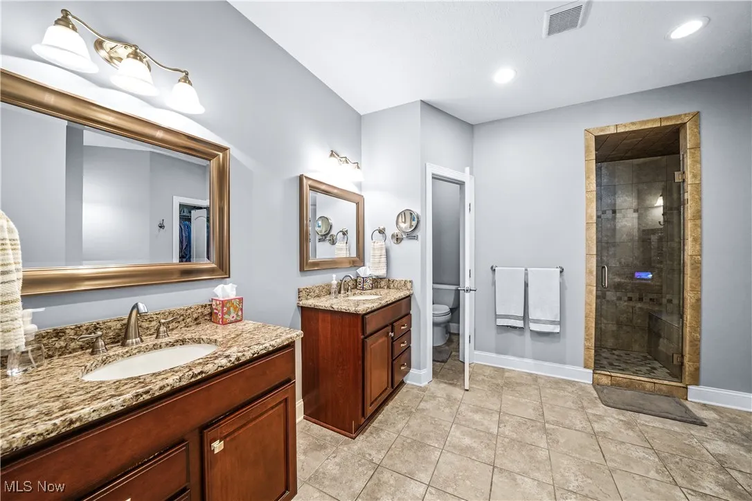 Full bathroom featuring a stall shower, toilet, baseboards, and two vanities