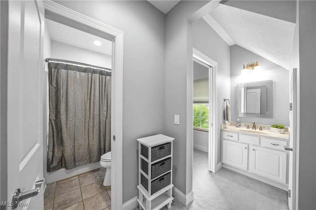 Full bathroom featuring vanity, toilet, vaulted ceiling, baseboards, and shower / bath combination with curtain