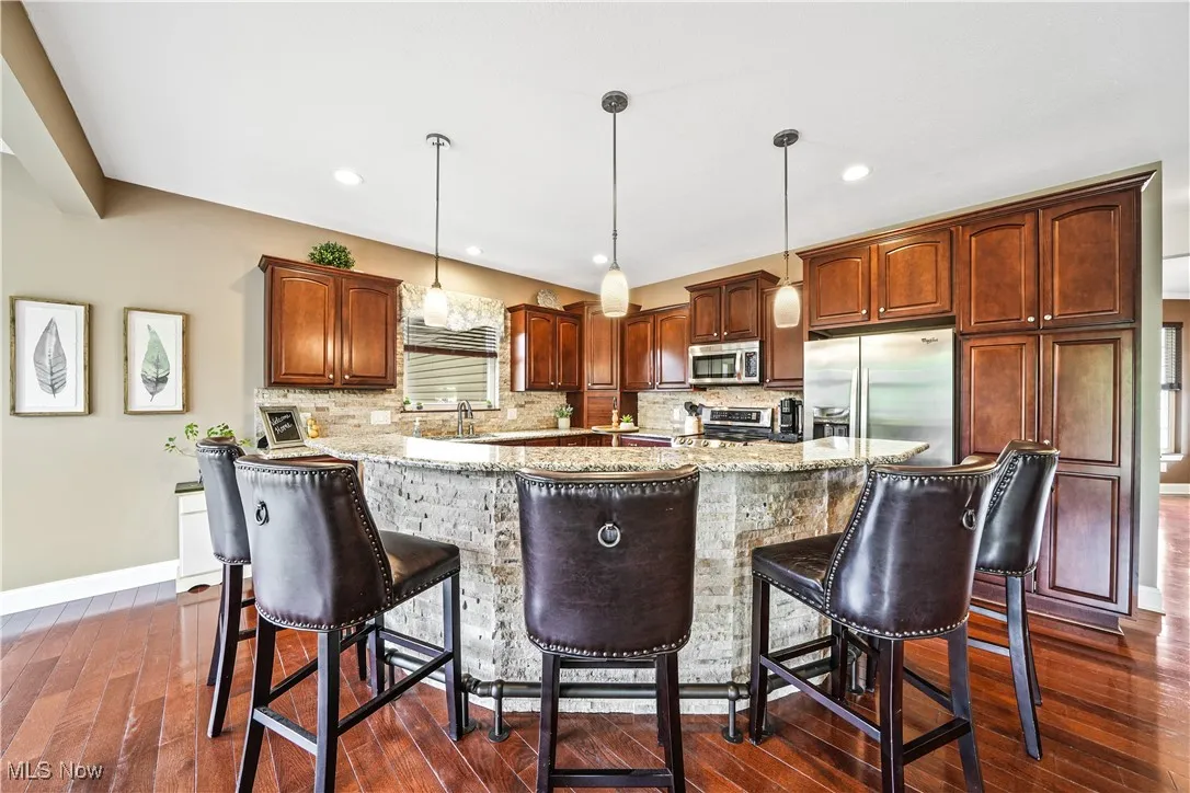 Kitchen with appliances with stainless steel finishes, dark wood-style floors, light stone countertops, decorative backsplash, and recessed lighting