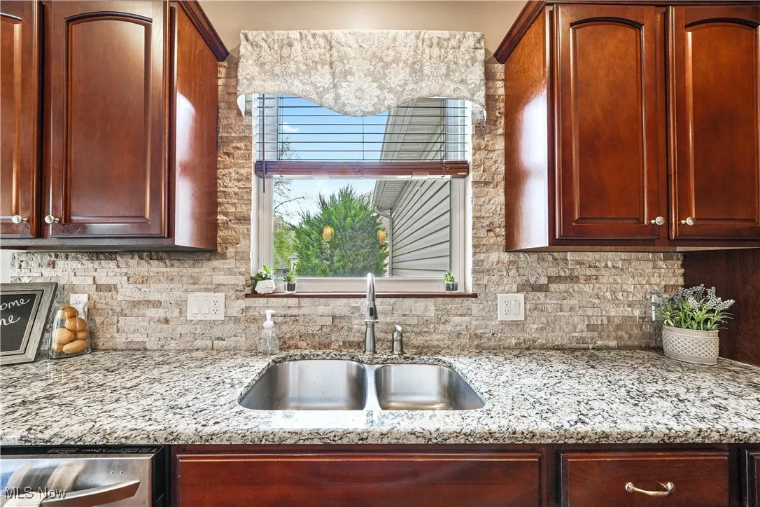 Kitchen with a sink, tasteful backsplash, light stone countertops, stainless steel dishwasher, and reddish brown cabinets