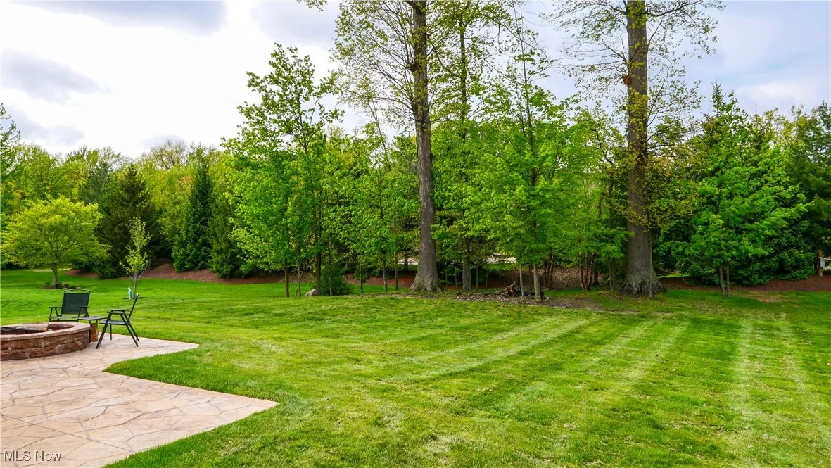 View of green lawn with an outdoor fire pit, a patio area, and view of scattered trees