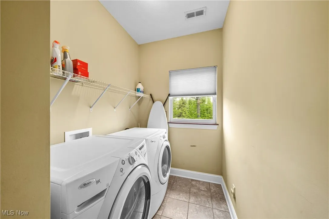 Clothes washing area with washing machine and clothes dryer, baseboards, and light tile patterned floors