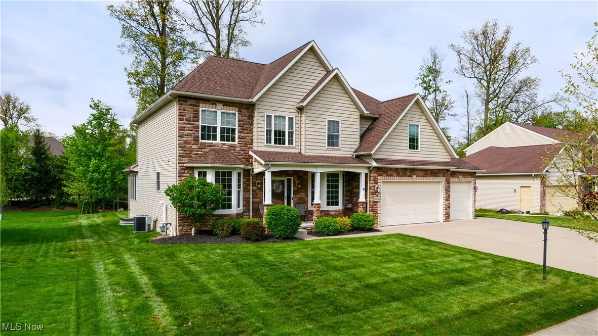 View of front facade featuring a porch, stone siding, concrete driveway, and a front yard