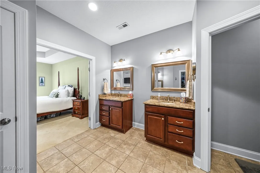 Bathroom featuring ensuite bathroom, two vanities, baseboards, and tile patterned flooring