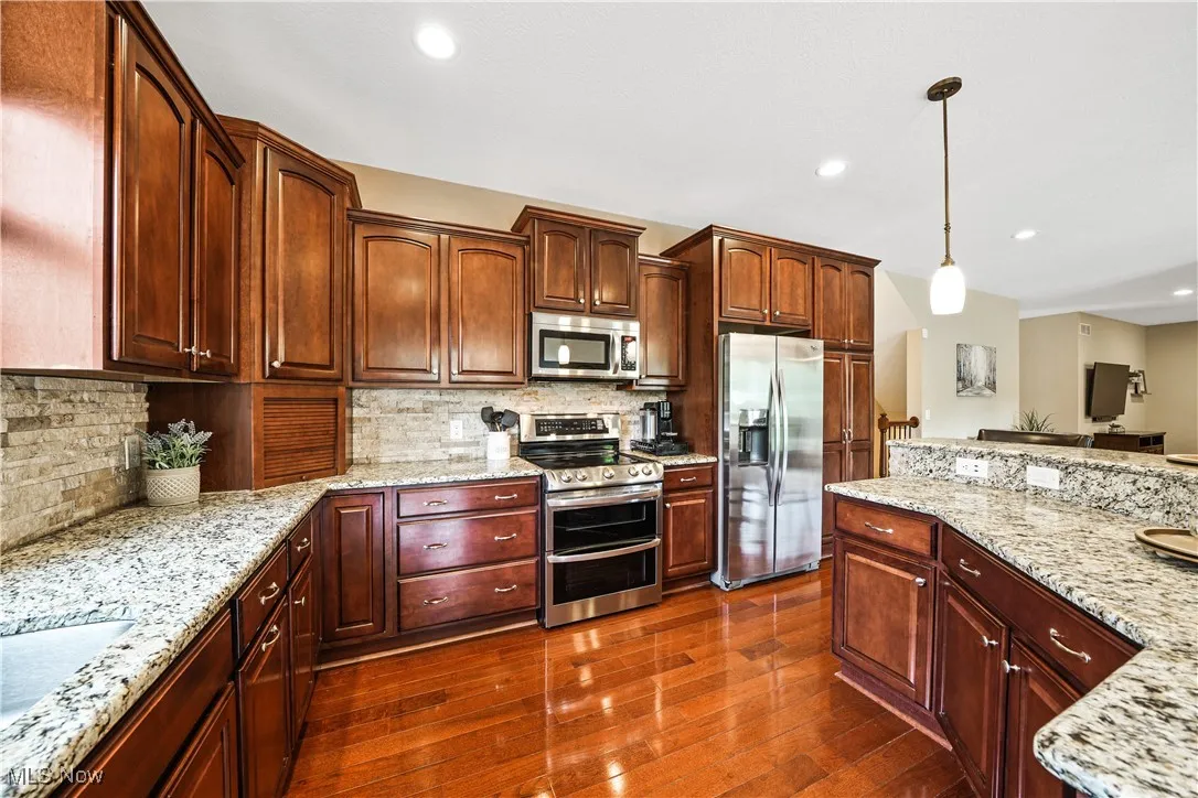 Kitchen with stainless steel appliances, pendant lighting, dark wood finished floors, light stone countertops, and recessed lighting