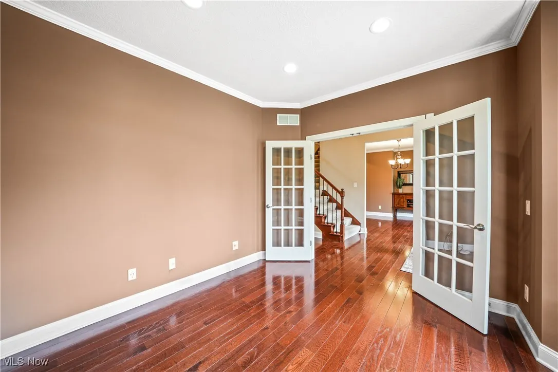 Unfurnished room featuring french doors, a chandelier, hardwood / wood-style flooring, baseboards, and ornamental molding