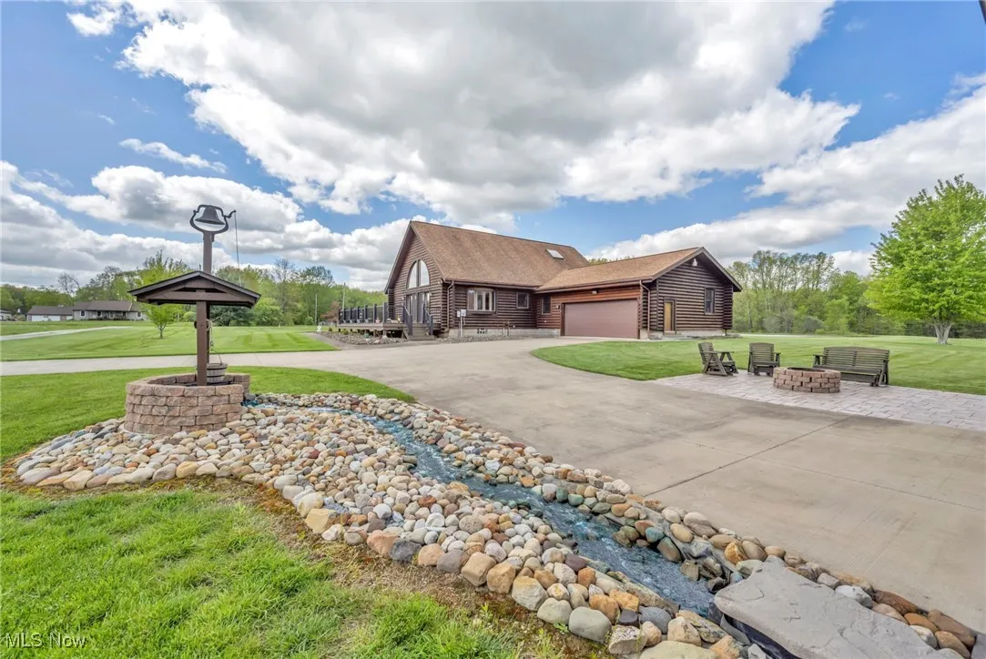 View of side of property with an outdoor fire pit, a front lawn, driveway, a garage, and a shingled roof
