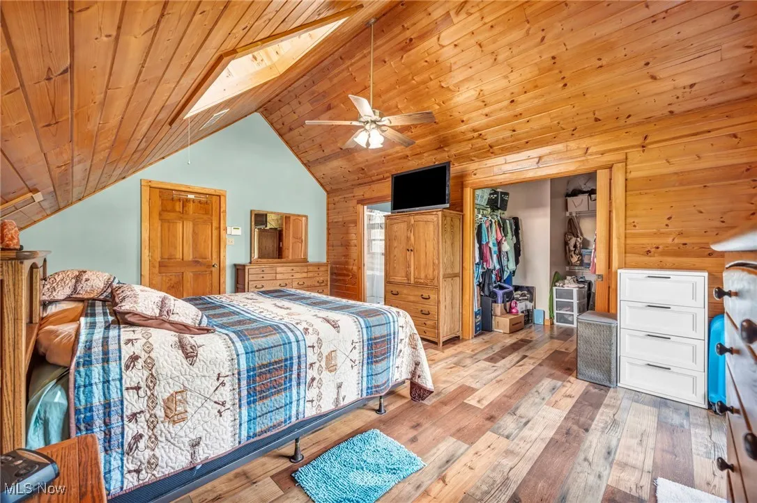 Bedroom with vaulted ceiling, wood-type flooring, wood ceiling, a closet, and wood walls